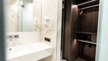 Ein modernes Badezimmer mit Marmorwaschbecken, einer in Glas abgeschlossenen Dusche und einem dunklen Holzwaschtisch mit integriertem Mikrowellenherd.