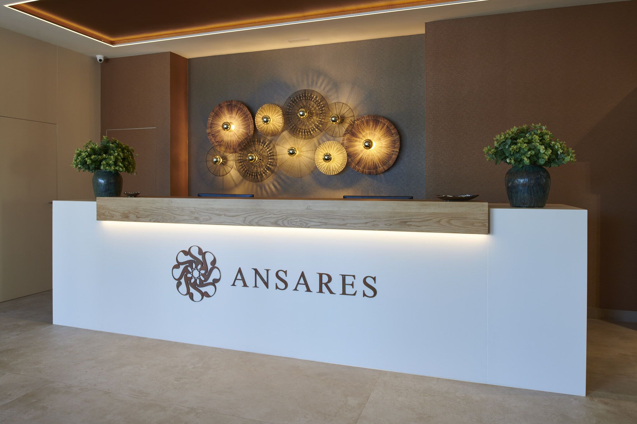 A reception desk with a logo, decorative wall art, and two potted plants.