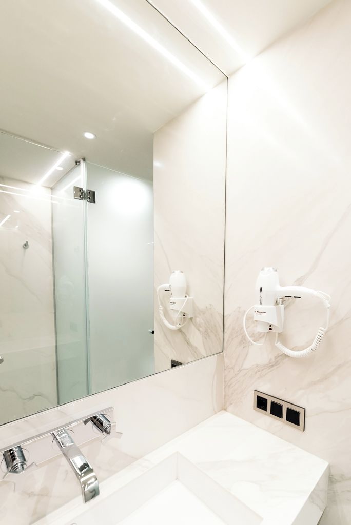 Een moderne badkamer met een grote spiegel, een witte wastafel en een haardroger die aan de muur is bevestigd.