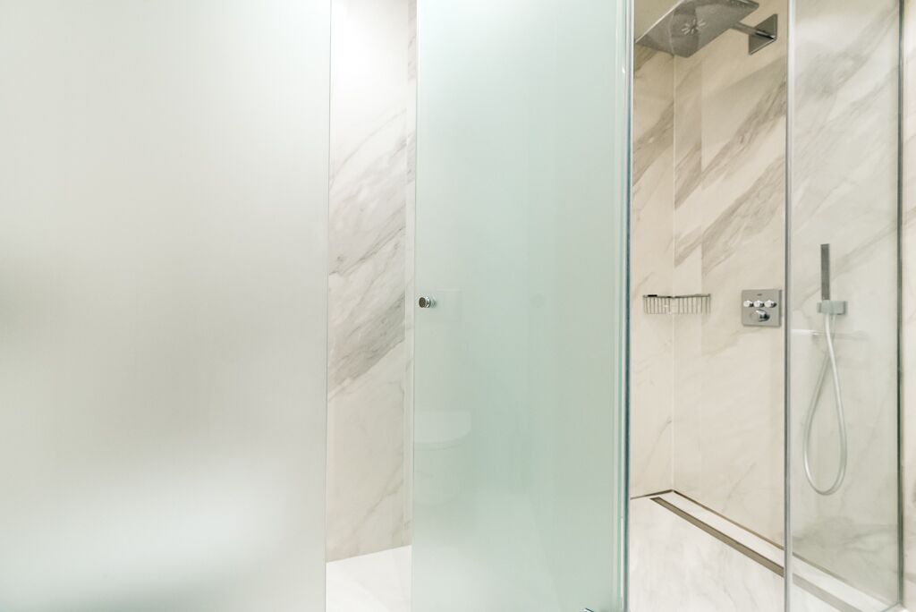A modern bathroom with a glass shower enclosure, marble tiles, and a visible control panel.