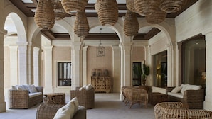 A spacious lounge area with wicker furniture, large windows, and a brick wall backdrop. - Ansares Hotel (Tarancon)