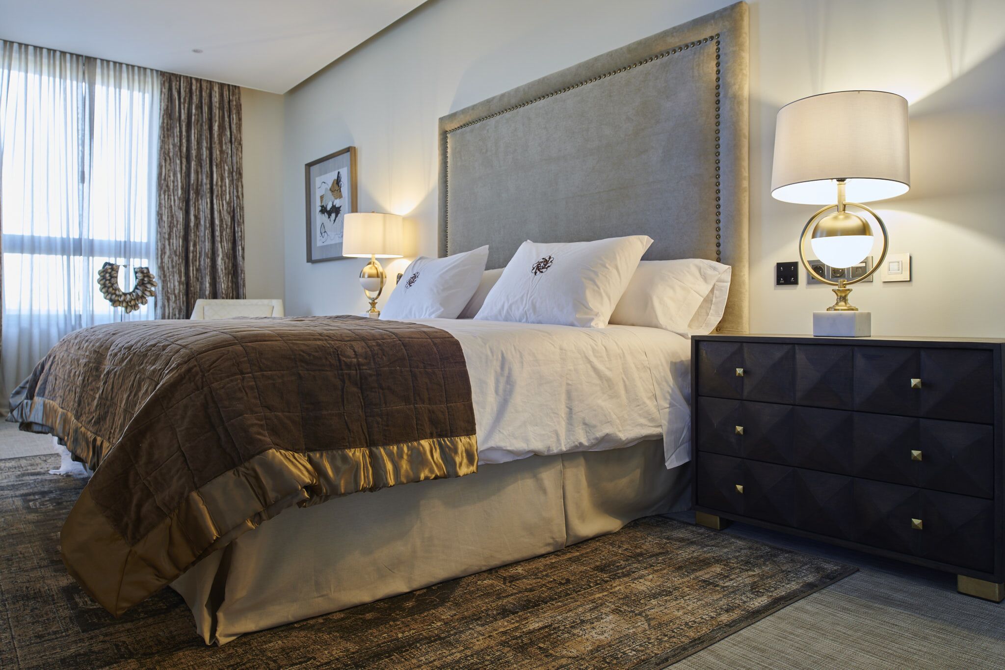 A hotel room with a large bed, a nightstand with a lamp, a dresser, and a framed picture on the wall.