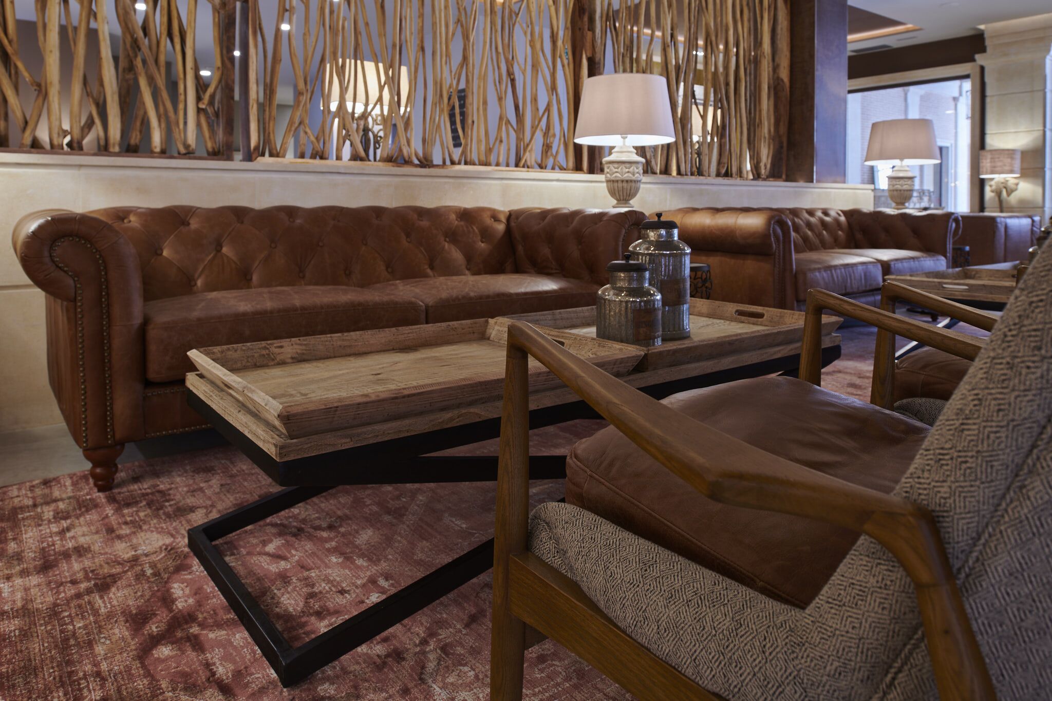A brown leather sofa, a wooden coffee table, and a patterned armchair in a room with a decorative wall and lamps.