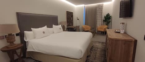 A hotel room with a large bed, a desk, two chairs, a television, and a plant.
