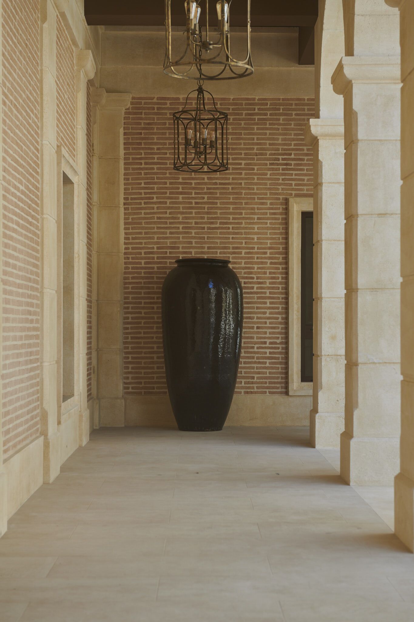 Un corridoio con un vaso nero grande, un muro in mattoni e un lampadario.