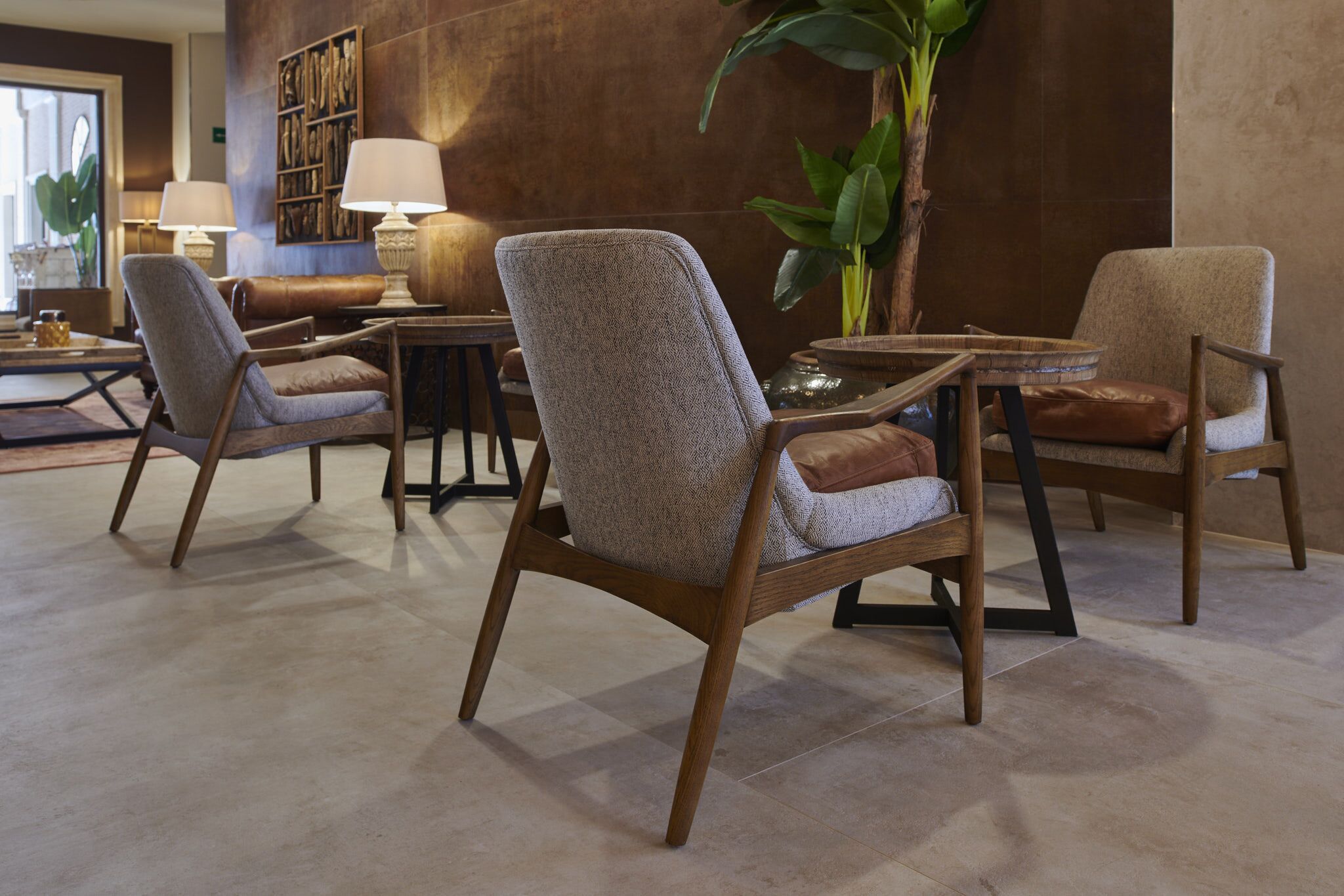 A modern lounge area with leather armchairs, a round table, and a large potted plant.