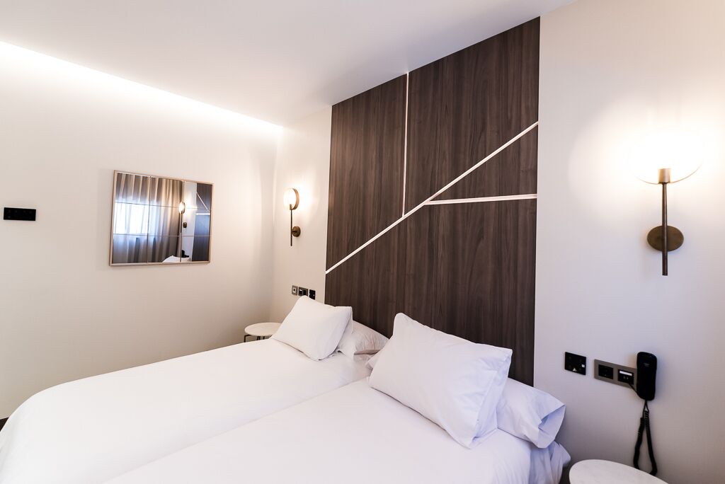 Una habitación de hotel moderna con una cama grande, un espejo y una lámpara de pared.