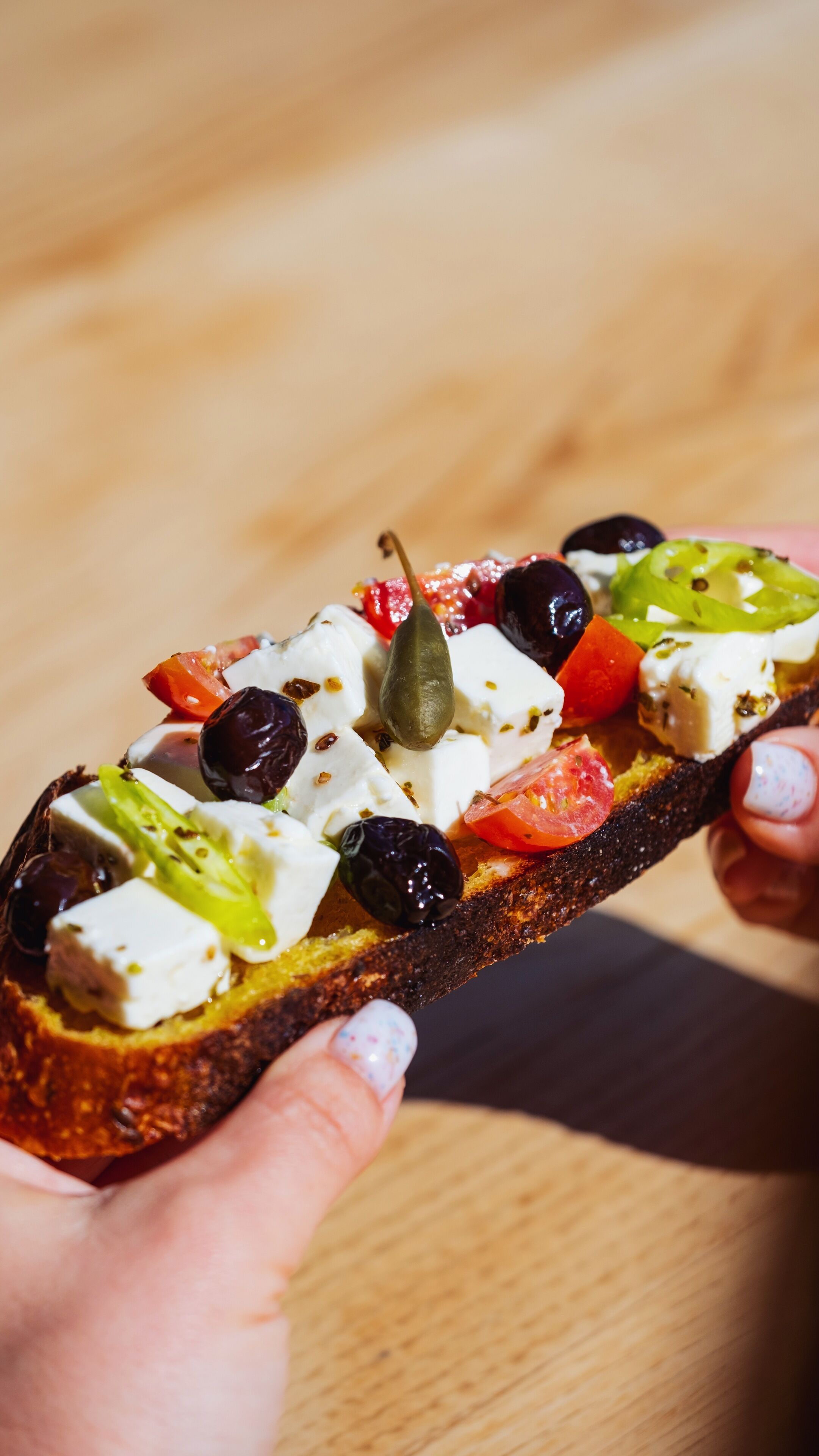 A close-up of a hand holding a slice of bread topped with various ingredients.