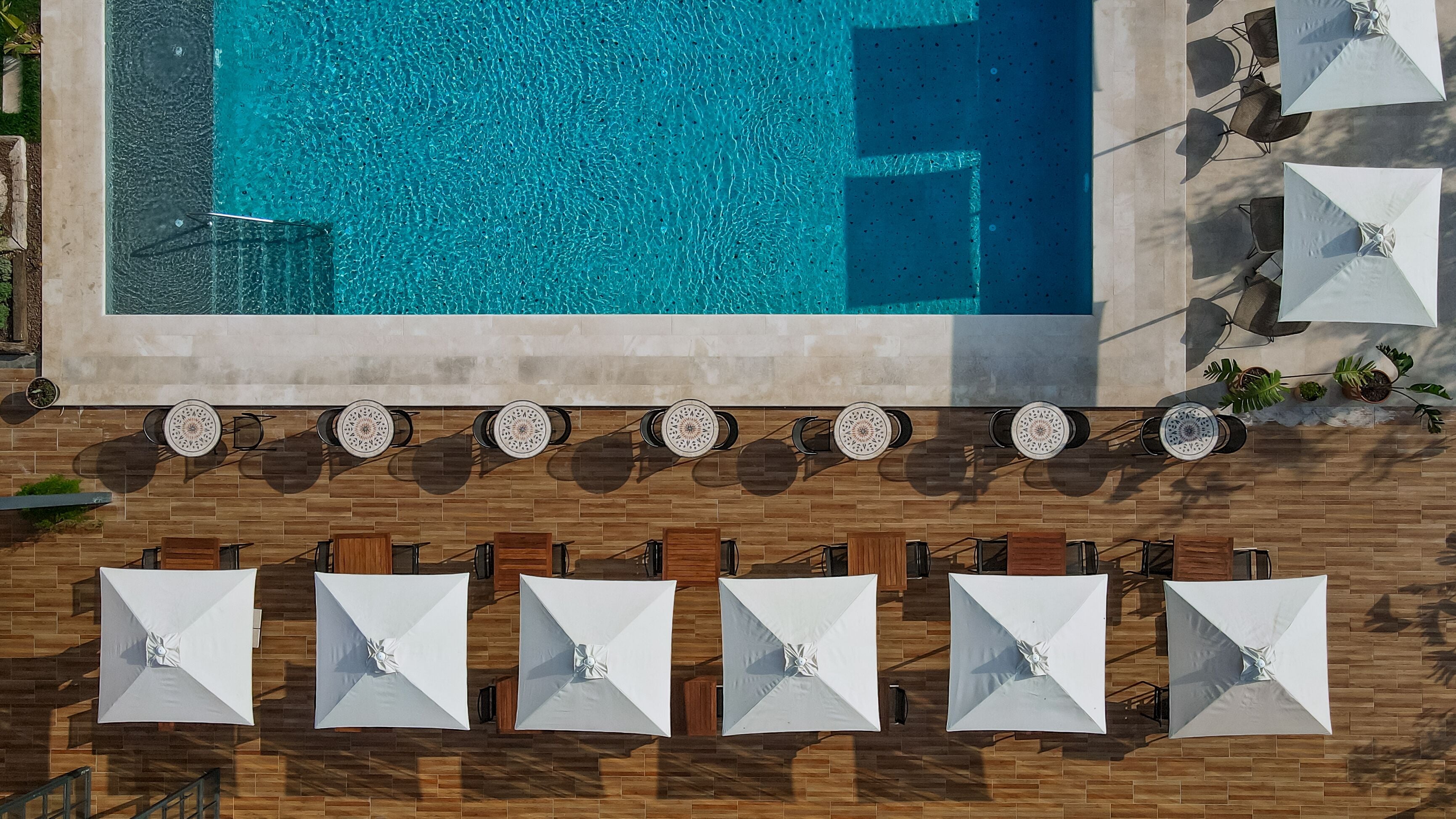 An aerial view of a pool area with a tiled deck, multiple umbrellas, and potted plants.