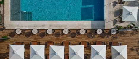 An aerial view of a pool area with a tiled deck, multiple umbrellas, and potted plants.