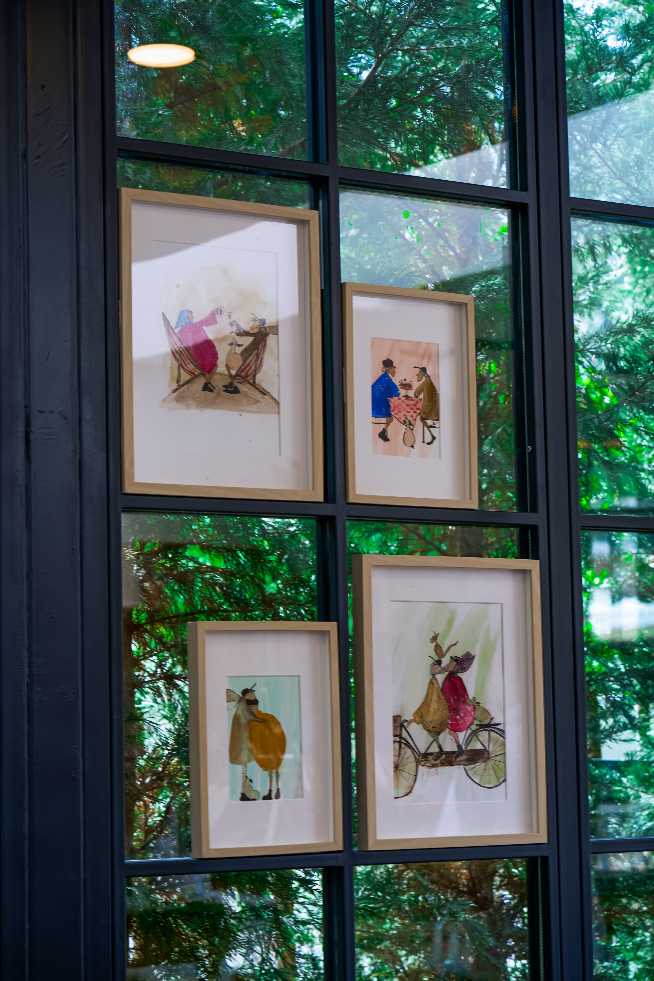 A window with four framed artworks depicting various scenes.