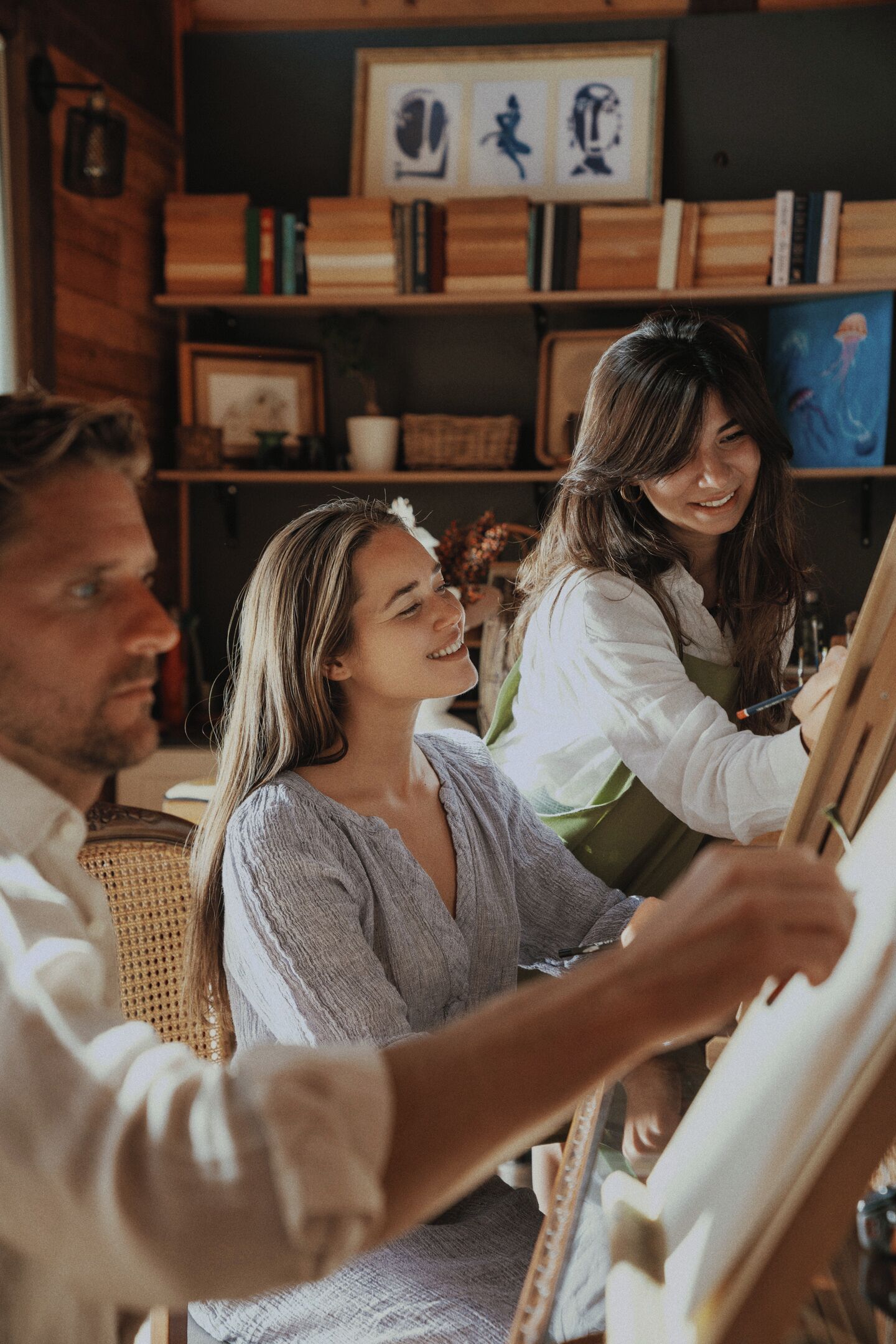 A room with a wooden bookshelf, a wicker chair, and a painting on the wall.