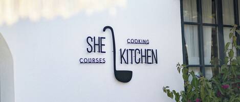 A white building with a sign that reads 'SHE COOKING KITCHEN COURSES.'