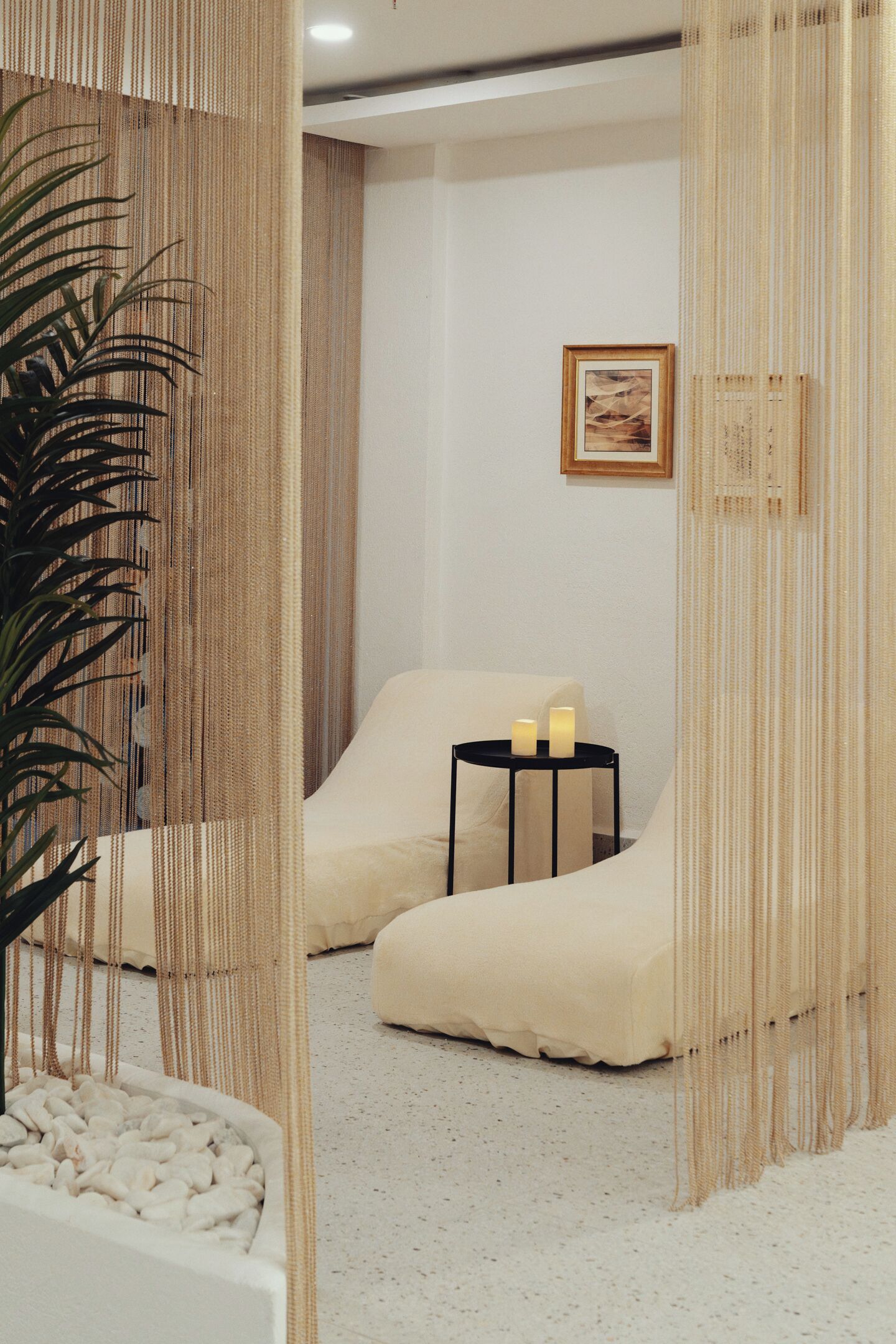Ein Spa-Raum mit einem weißen, gepolsterten Sessel, einem kleinen schwarzen Tisch mit Kerzen und einem gerahmten Bild an der Wand.