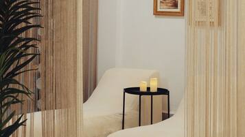 Ein Spa-Raum mit einem weißen, gepolsterten Sessel, einem kleinen schwarzen Tisch mit Kerzen und einem gerahmten Bild an der Wand.