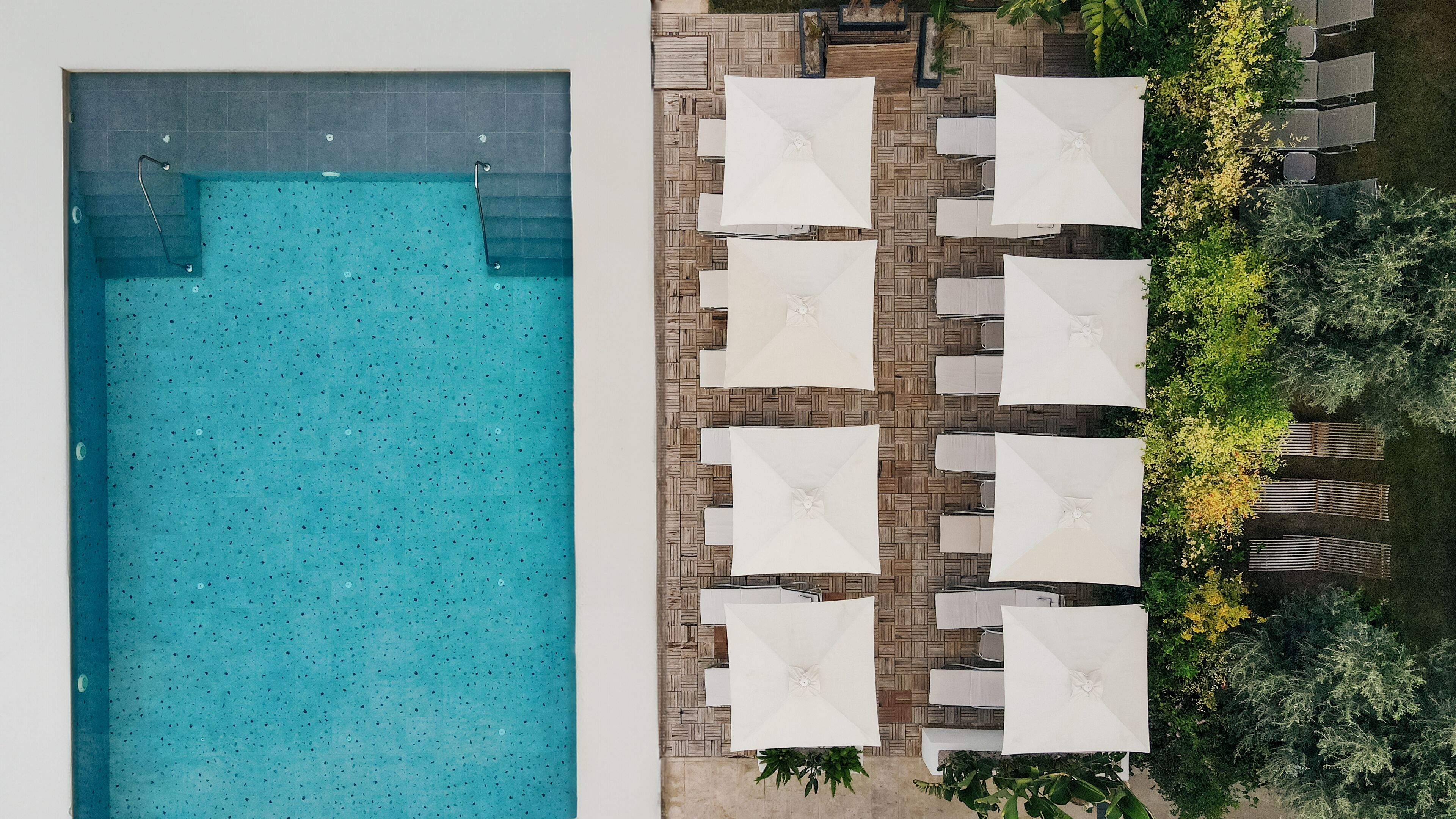Vue aérienne d’une piscine dotée d’une terrasse carrelée et de parasols blancs.