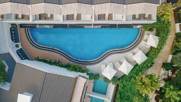 Vista aérea de un hotel con una gran piscina central, varias áreas de descanso con sombrillas y un jardín bien cuidado.