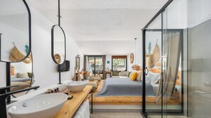 Een moderne slaapkamer met een groot bed, een houten nachtkastje met een witte kom, een spiegel met een zwart frame en een douchecabine met glazen wanden.