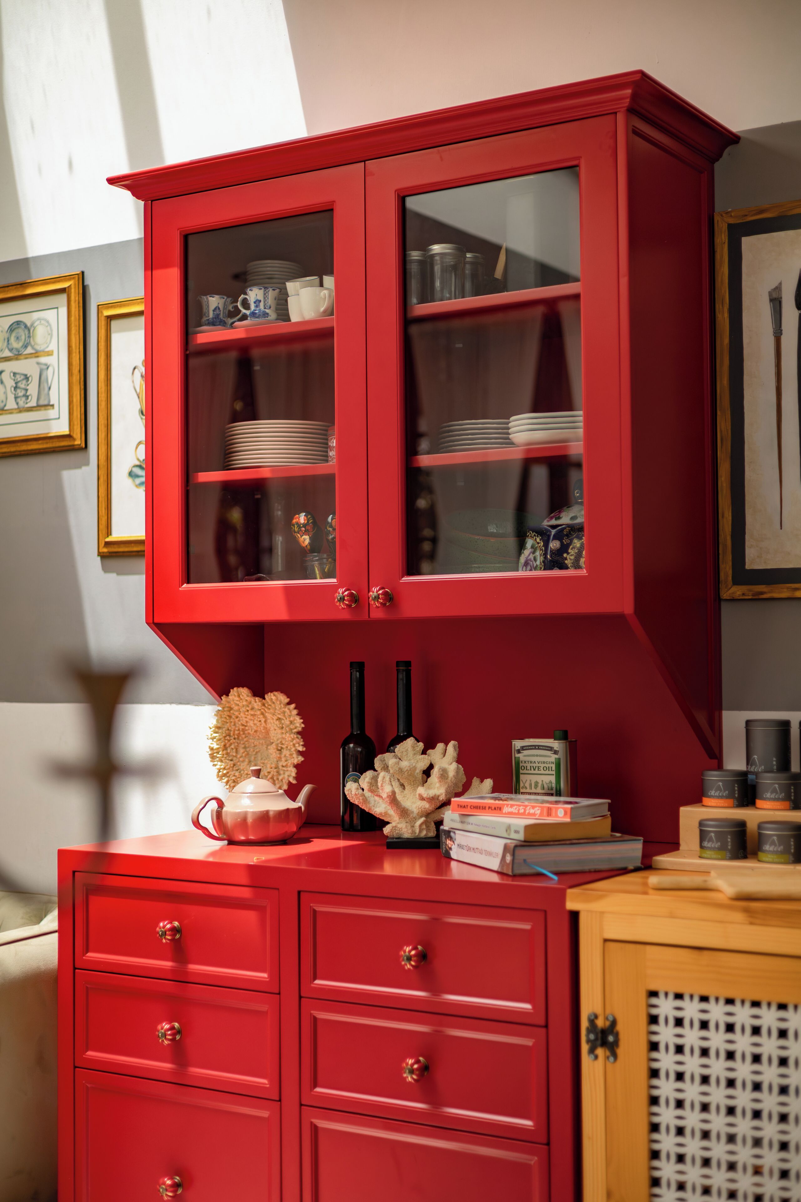 A red cabinet with glass doors, drawers, and a shelf with books and bottles.