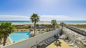 A pool area with a view of the beach and ocean, surrounded by palm trees and lounge chairs. - Seacrest 301AB is a 3 BR Gulf front on Okaloosa Island by RedAwning (Fort Walton Beach)