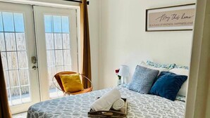 A bedroom with a bed, a chair, a bedside table with a lamp, and a door leading to a balcony. - Experience the passion of hospitality, cleaning, and good location! (Tampa)