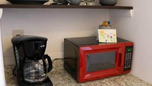 A kitchen with a coffee maker, a red microwave, and a shelf with cups and bowls. - Experience the passion of hospitality, cleaning, and good location! (Tampa)