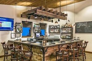 Una zona de bar con taburetes de madera, una barra con caja registradora y estanterías llenas de botellas.