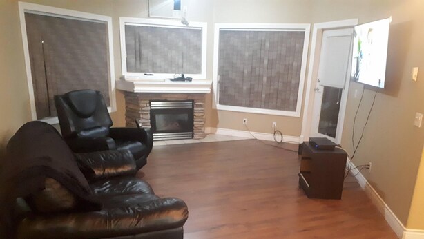 A living room with a fireplace, a black leather sofa, a TV, and a flat-screen TV mounted on the wall.