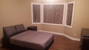 A bedroom with a bed, nightstands, and a dresser. There are three windows with curtains.
