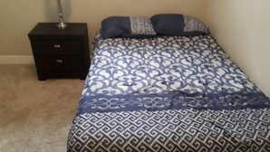 A bedroom with a bed, a nightstand, and a lamp. - Heritage 2 Bedroom Deluxe Apartment (Fort McMurray)