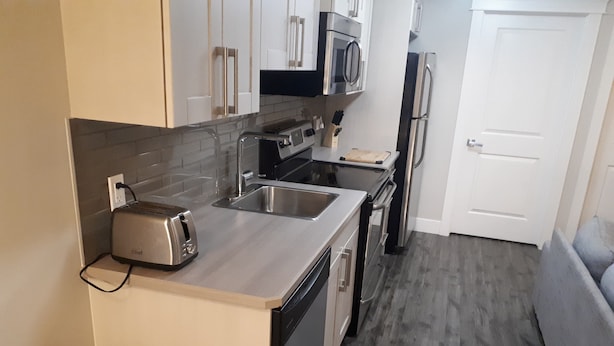 A compact kitchen with a toaster, sink, microwave, and refrigerator. - Heritage 2 Bedroom Deluxe Apartment (Fort McMurray)