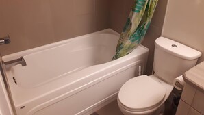 A bathroom with a bathtub, toilet, and shower curtain. - Heritage 2 Bedroom Deluxe Apartment (Fort McMurray)