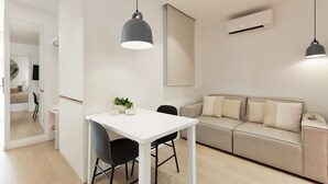 Ein moderner Wohnraum mit einem weißen Esstisch, schwarzen Stühlen, einem beigen Sofa und Pendelleuchten.