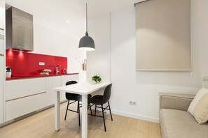 Une cuisine moderne avec des meubles blancs, un plan de travail rouge et une suspension noire au-dessus de la table à manger.