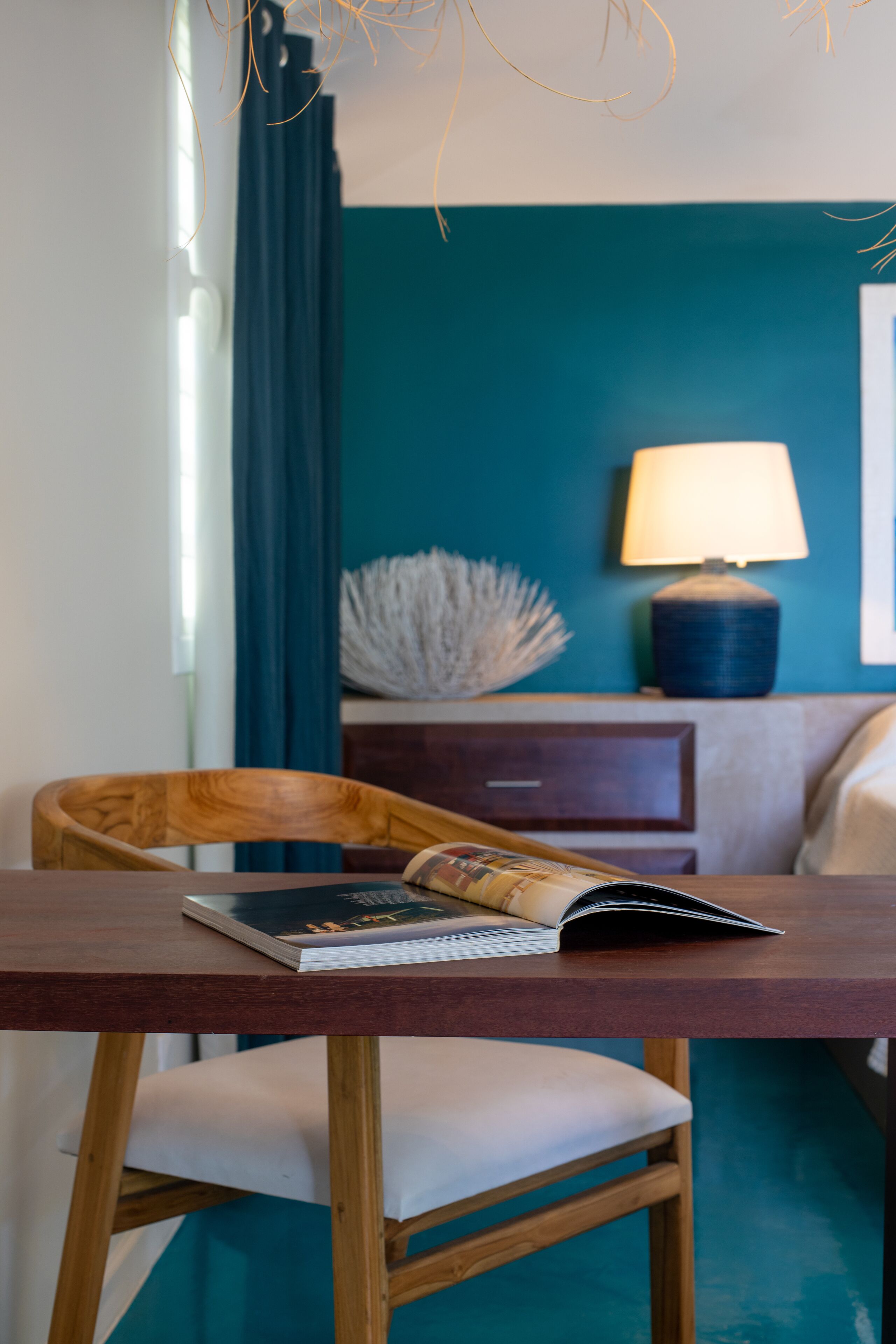 A room with a wooden table, a chair, a lamp, a nightstand, and a bed.