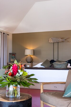 A hotel room with a bed, a bedside lamp, a decorative wall piece, a vase with flowers, and a chair.