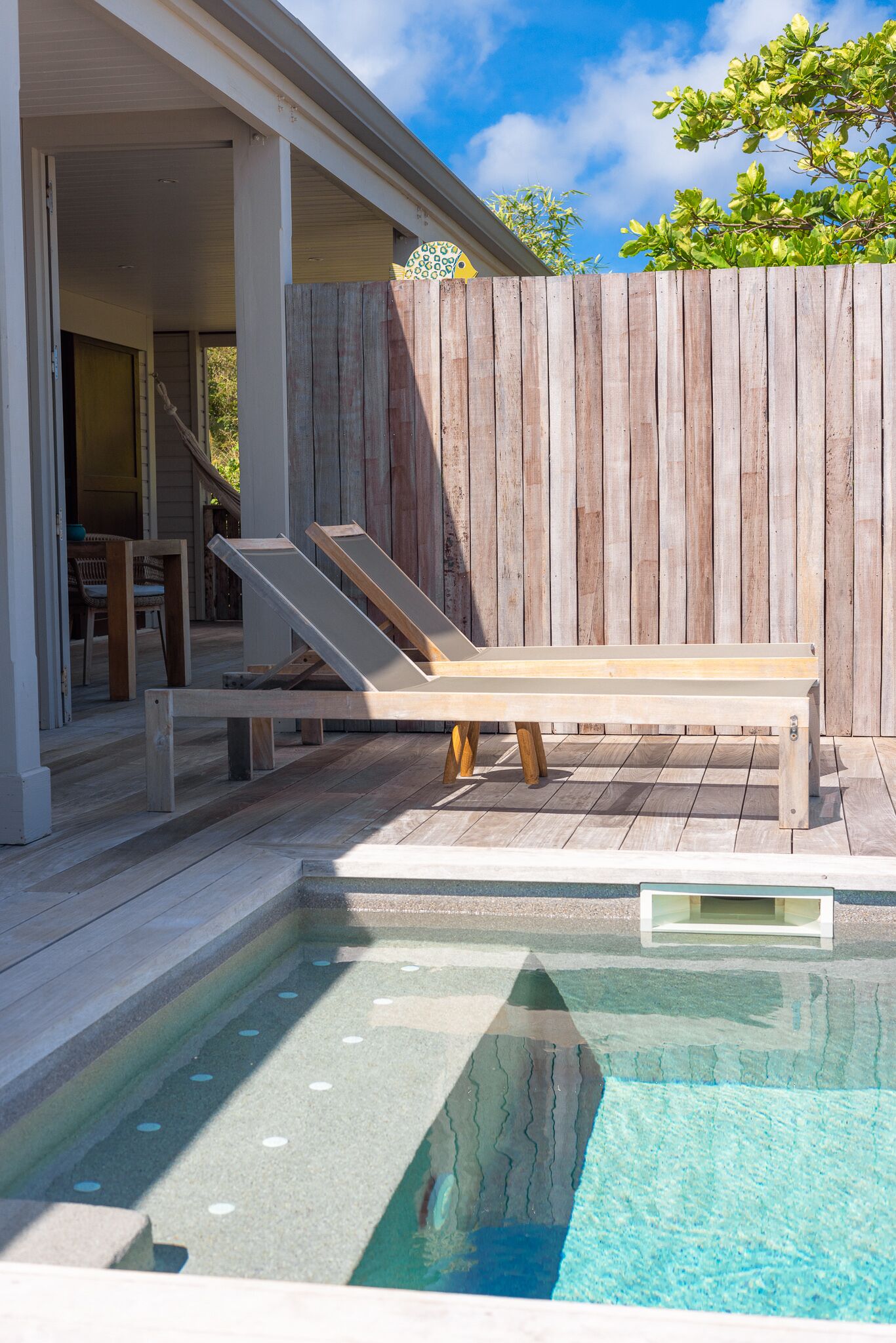 A wooden deck with a pool, a lounge chair, and a wooden fence.