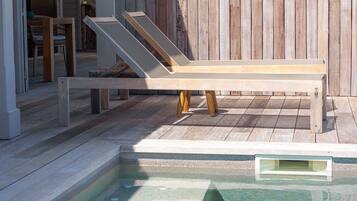 A wooden deck with a pool, a lounge chair, and a wooden fence.