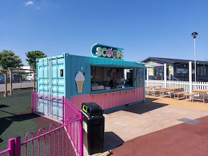 A Scoops ice cream truck with a pink fence and a trash bin in front.
