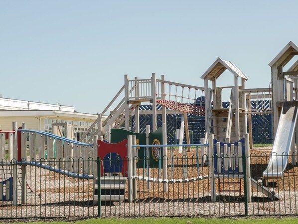 A playground with various play structures including slides, climbing areas, and a fenced play area.