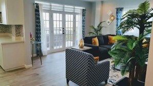 Ein modernes Wohnzimmer mit einer schwarzen Couch, einem gemusterten Sessel und einer großen Topfpflanze.