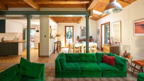 Amplia sala de estar con un juego de sofá verde, vigas de madera en el techo y un comedor con mesa y sillas.