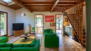 Amplia sala de estar con techo de madera, sofás verdes, un televisor y un comedor con mesa y sillas.
