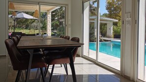Zona pranzo con un tavolo grande e sedie, vista su una piscina e un'area salotto esterna coperta.