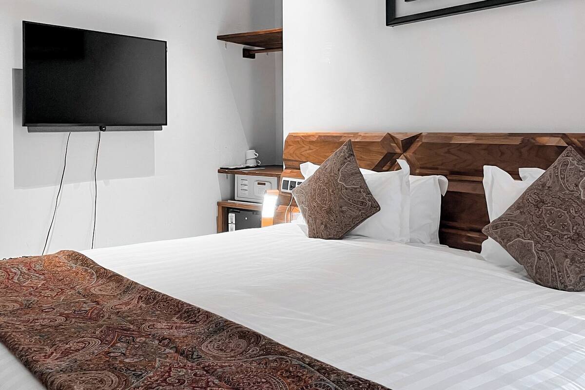 Una habitación de hotel moderna con una cama grande, un televisor de pantalla plana montado en la pared, un cabecero de madera y una alfombra decorativa.