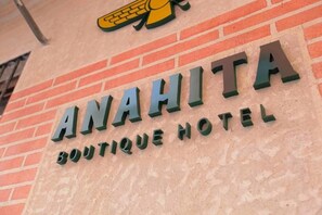 Une enseigne pour l’hôtel-boutique Anahita, avec un logo représentant un oiseau stylisé placé au-dessus du texte.