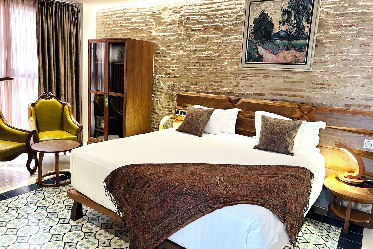 Habitación de hotel con una cama grande, un armario, una silla y un cuadro en la pared.