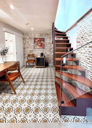 Un intérieur moderne avec un sol à motifs, une table à manger en bois, une chaise, un petit meuble et un escalier doté d’une rambarde en verre.