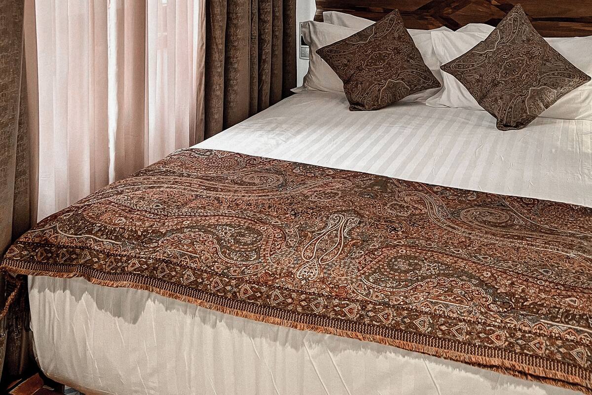Una cama bien hecha con un edredón estampado, un cabecero de madera y tres almohadones decorativos.