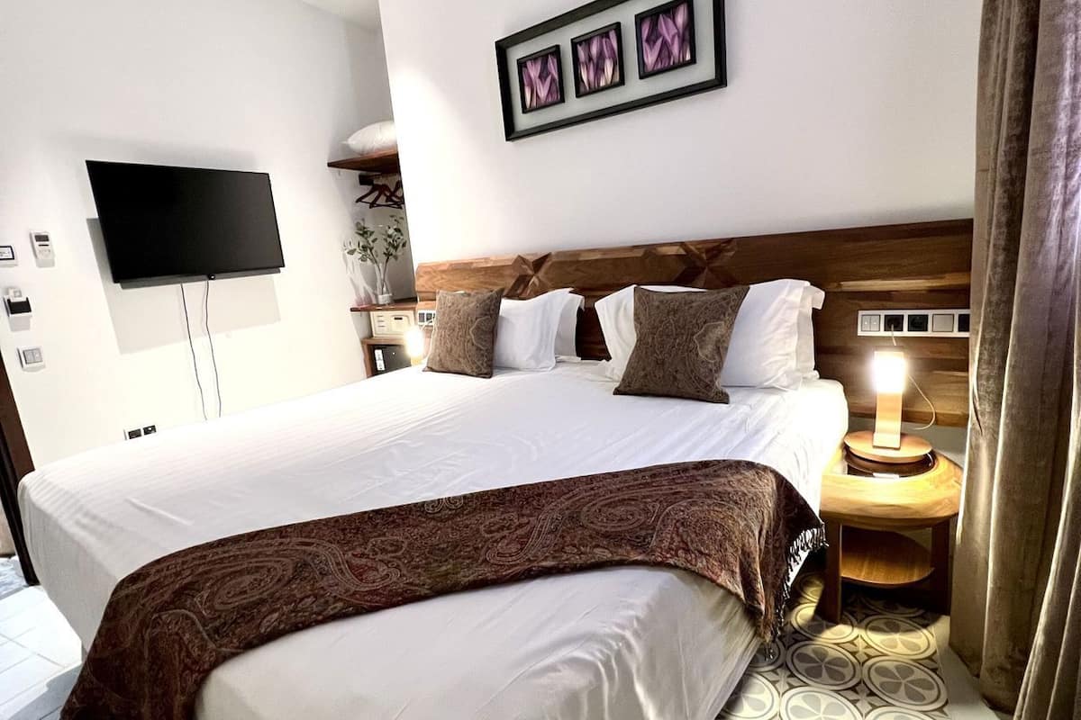 Habitación de hotel con una cama grande, un televisor de pantalla plana en la pared, cabecera de madera y piso con estampado.